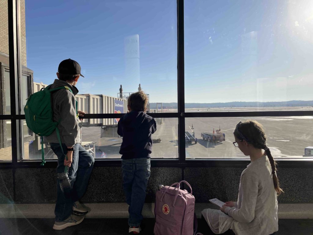 Two children watching planes at an airport while third reads